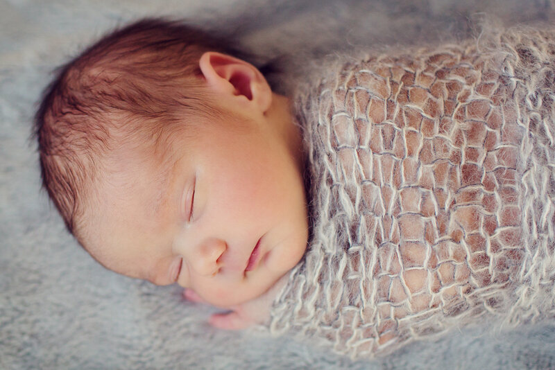 Newborn snuggled into a hand knot wrap, sleeping soundly and shot from above.
