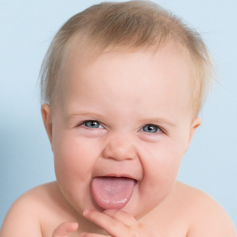 Smiling baby with tongue out against a blue background – milestone session in Lancaster, PA