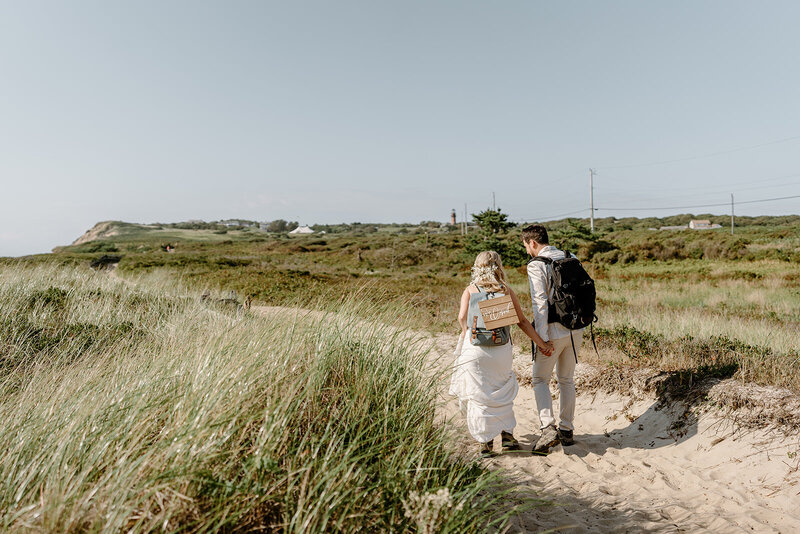 wedding couple with hiking backpacks exiting beach