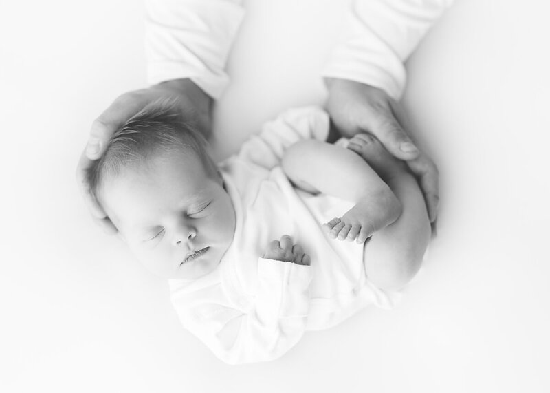 black and white picture of a baby gently held in mom and dads hands