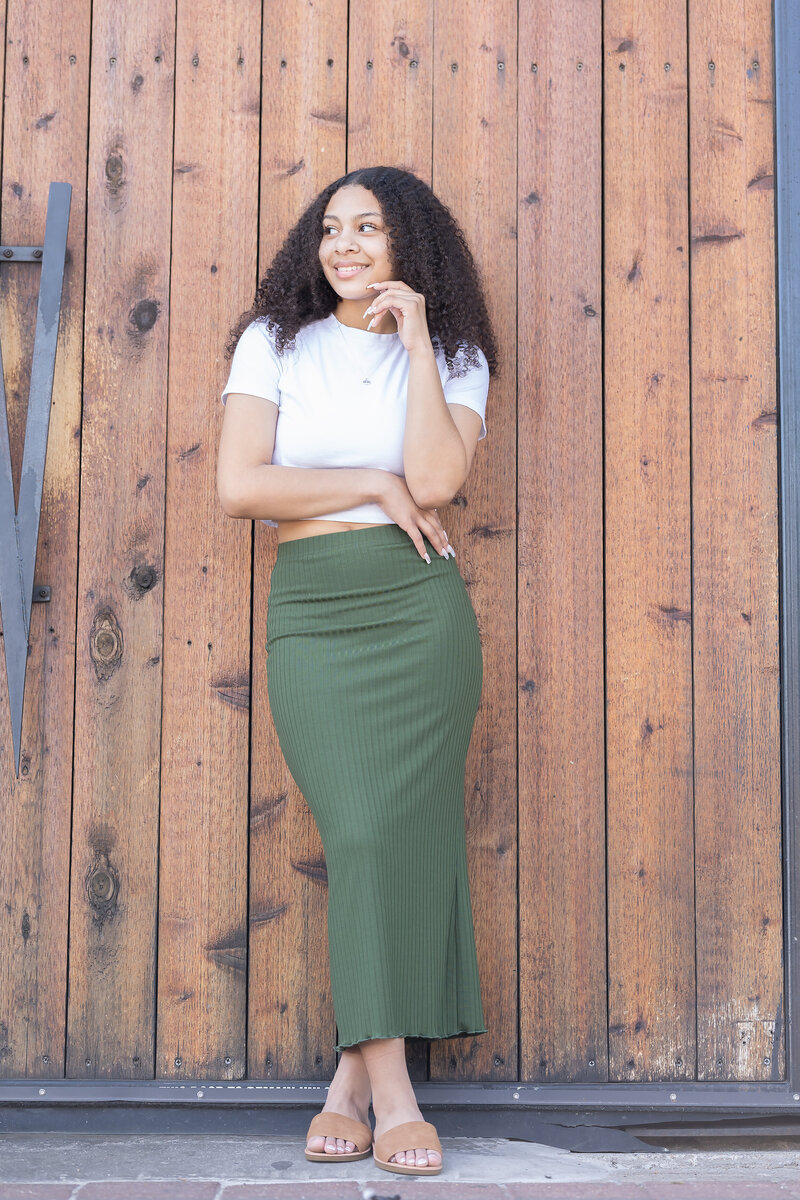 Senior portrait of woman in white top and green skirt in Dallas, TX