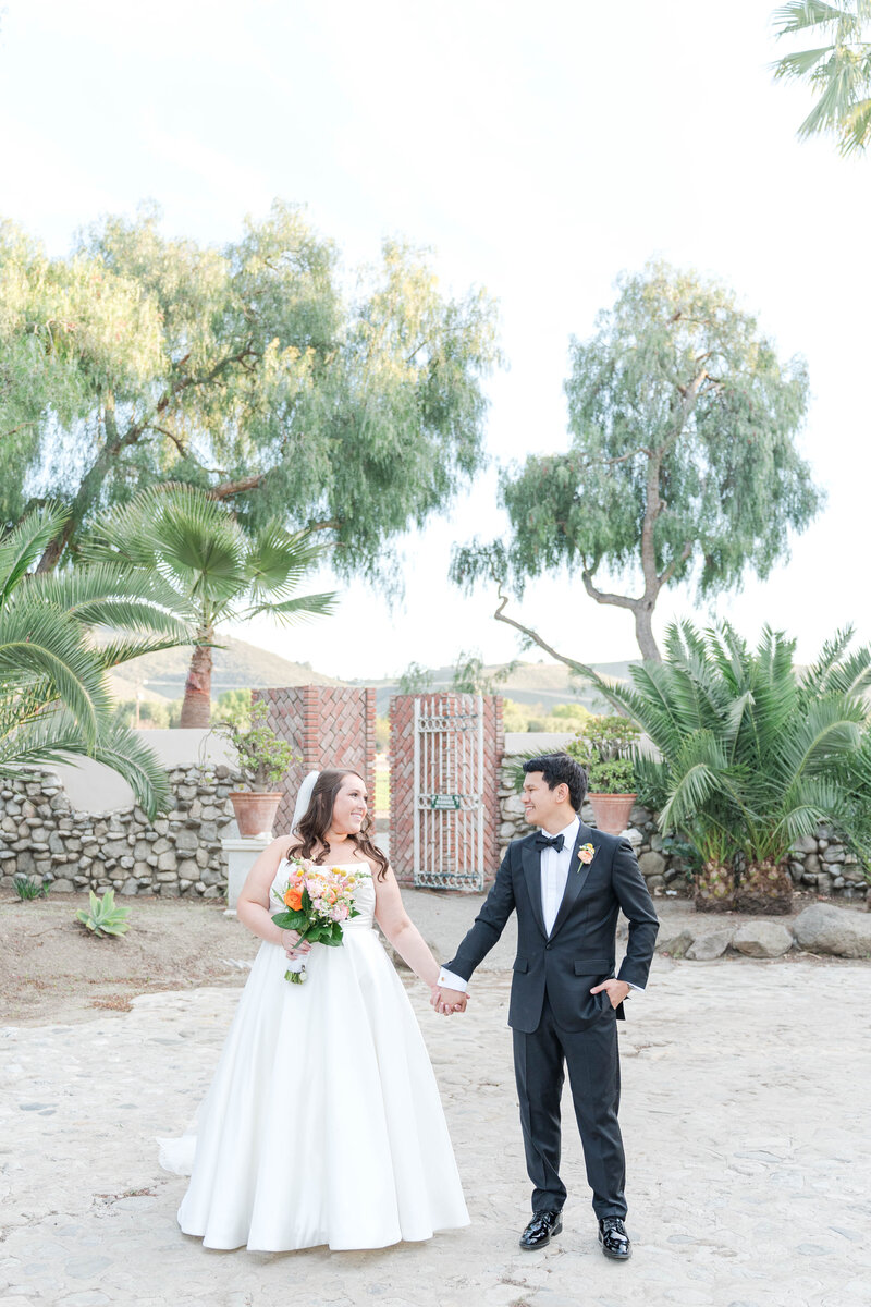 Bride and groom holding hands at Rancho de las Palmas, surrounded by palm trees