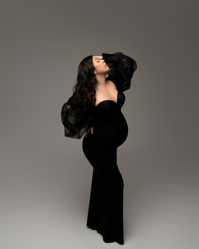 Dramatic pose in a curve-hugging black gown with sheer statement sleeves