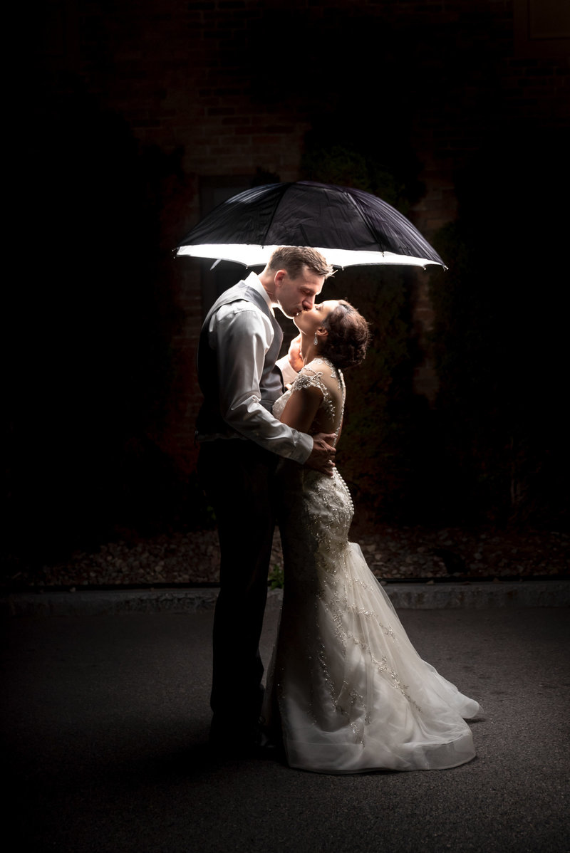 Bride and groom kiss under and umbrella