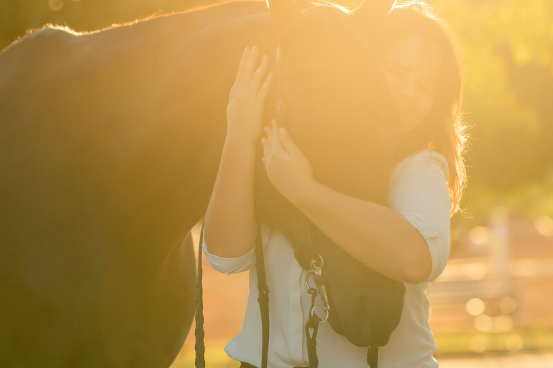 In a sunny close up image, a brunette high school senior hugs her Off the Track Thoroughbred Ser for her High School Senior photos with her horse