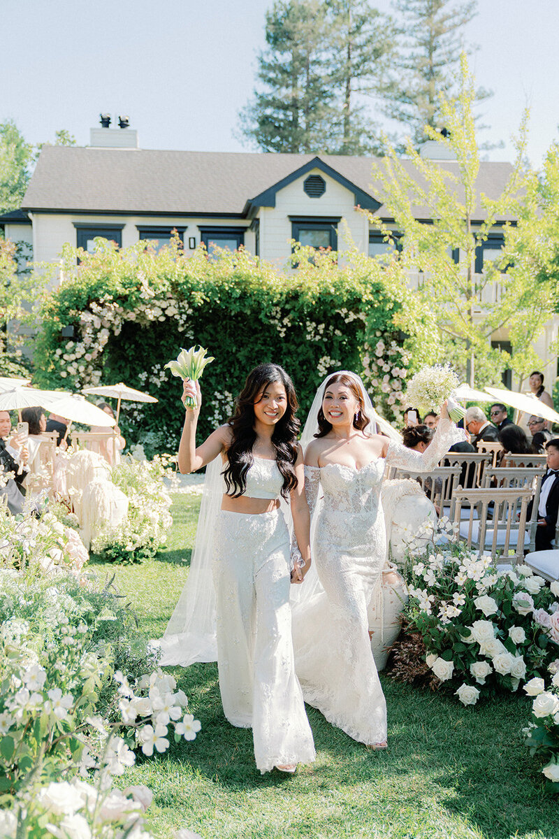 two brides walking down the aisle smiling at the camera