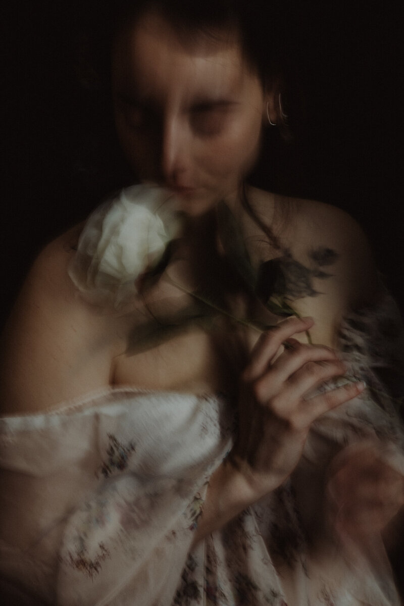 Donna con peonia bianca sul petto, sguardo rivolto all’obiettivo, illuminata da luce naturale morbida.