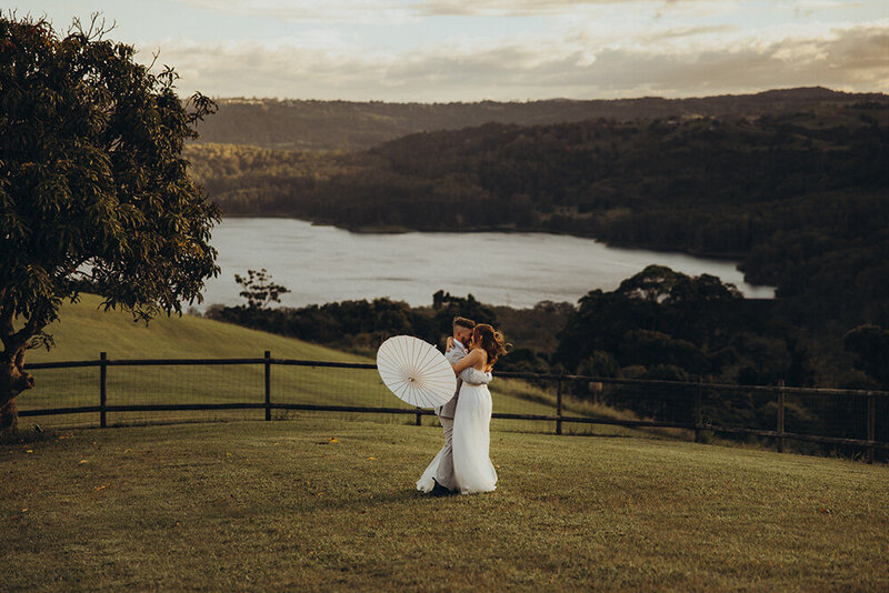 Adventurous elopement in Sunshine Coast open field bride and groom embracing while holding parasol