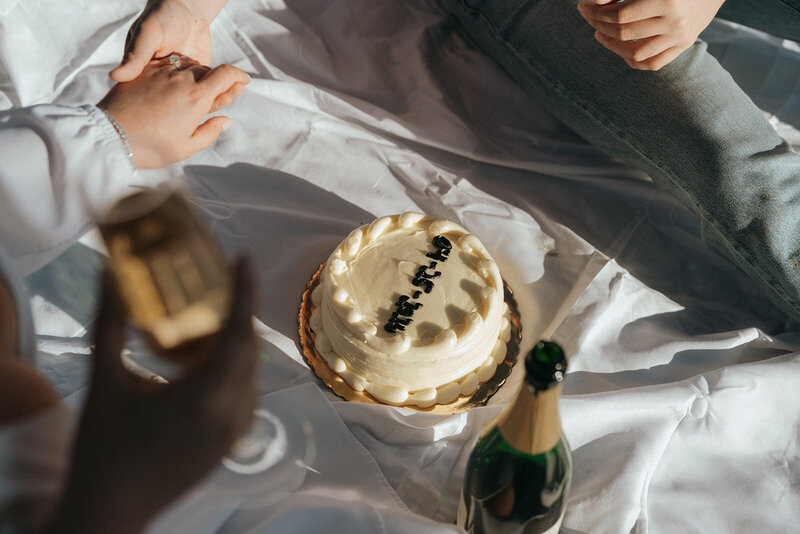 couple sharing cake and champagne during engagement photos, captured by Elsie Goodman, an NYC engagement and couples photographer