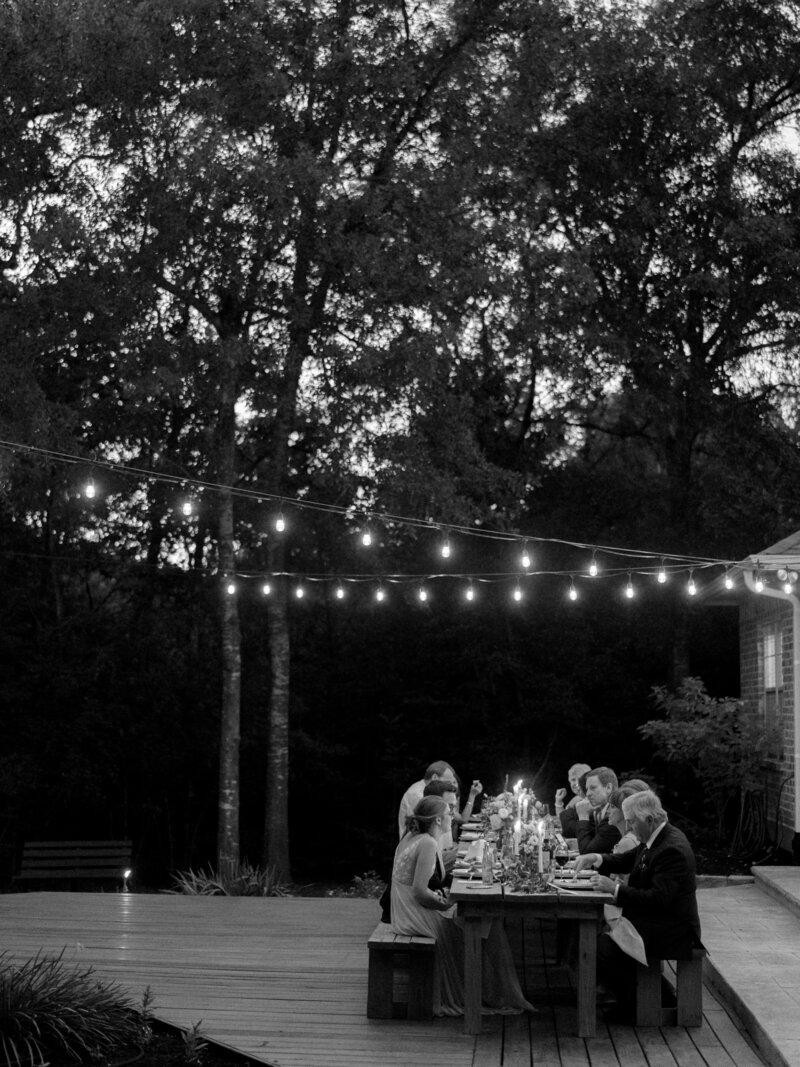 Black and white image of people sitting at a reception table under string lights