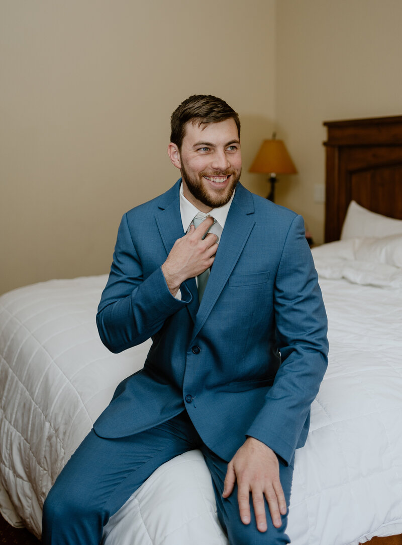       Groom preparing for his wedding day in a Vail hotel room, surrounded by elegant details and mountain views outside the window