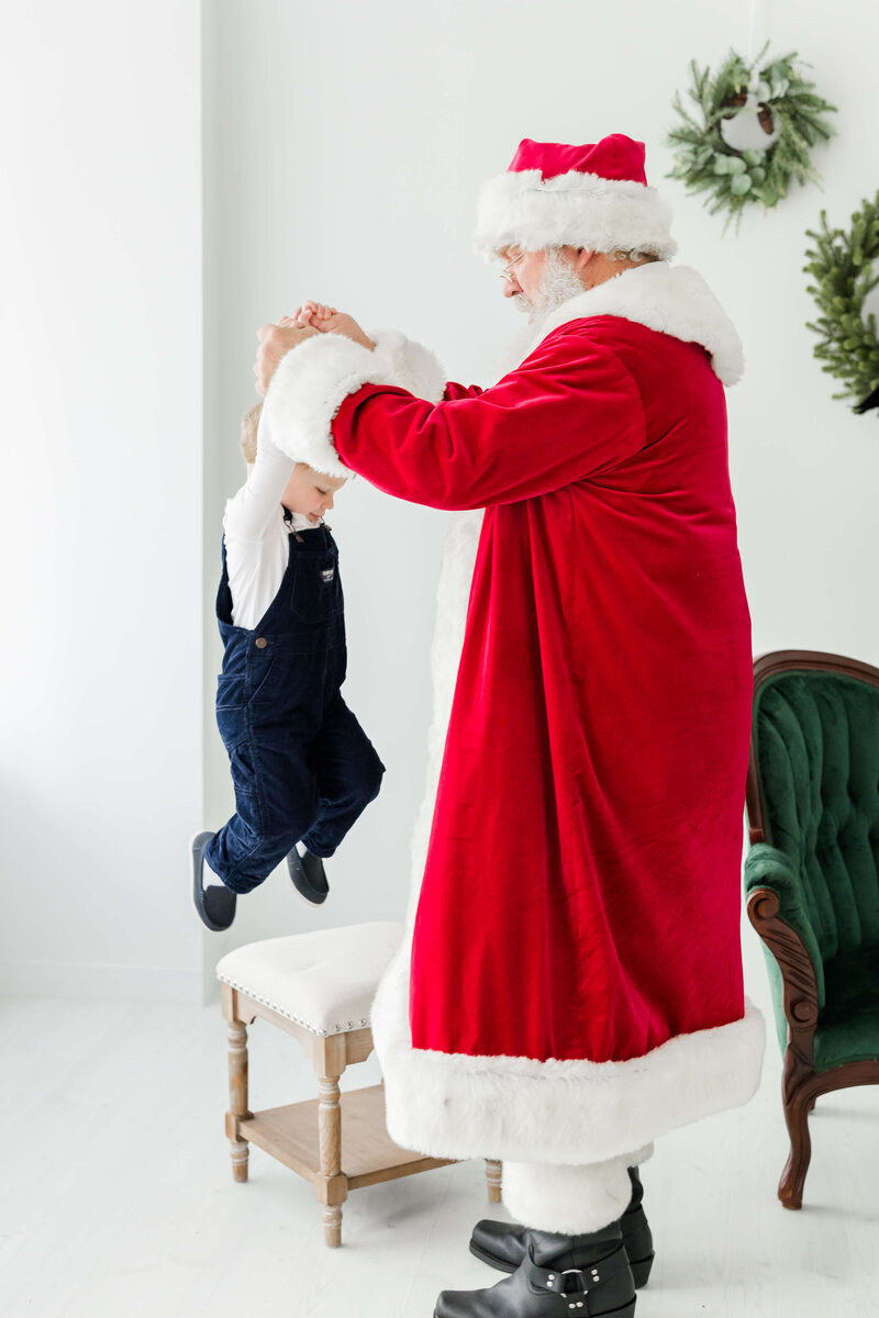 Child holding santas hand and jumping during santa mini session