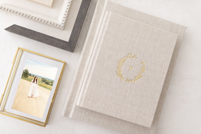 Flatlay of heirloom photo albums, frames, and a printed portrait from a Kansas City maternity session, styled for gallery review day.