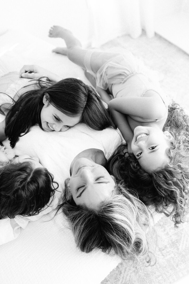 Black and white image of Mother with three daughters laying on bed during family photo session
