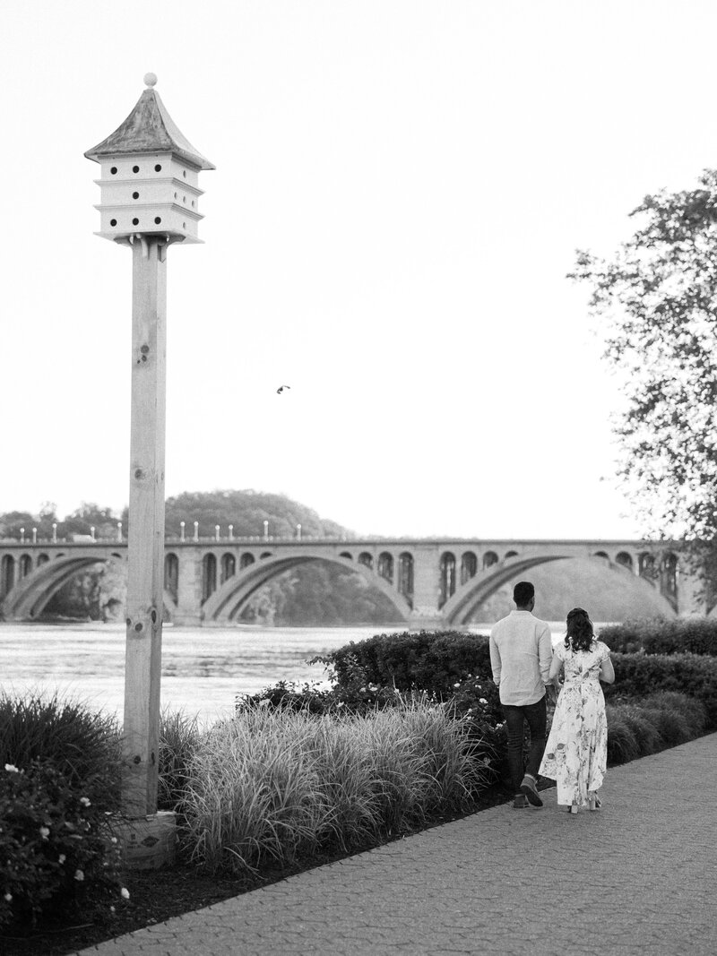 A couple walks away down the waterfront path in georgetown, washington dc with the fraqncis scott key bridge in the background