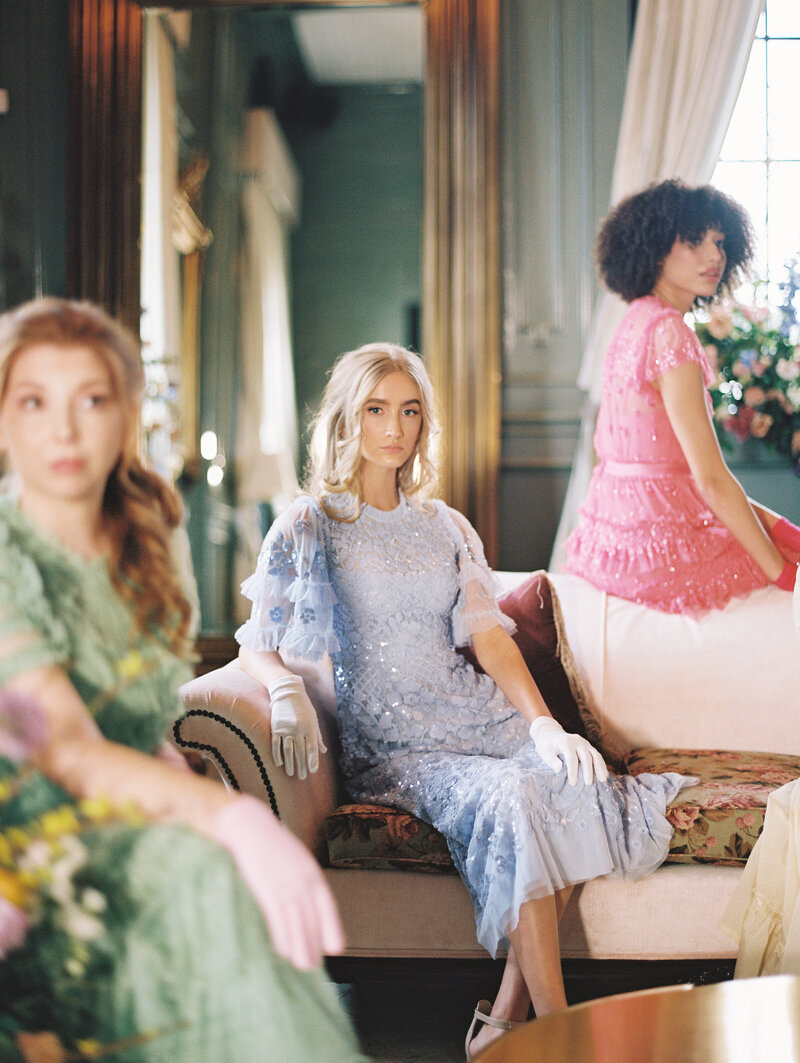 Three women in pastel colored dresses sit on a fancy couch