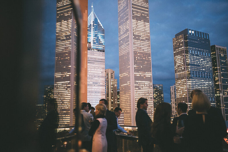 Chic rooftop wedding reception with guests mingling against a breathtaking city skyline at dusk.