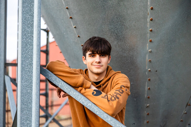 Senior guy standing near farm equipment during a De Soto, Missouri senior session. 
