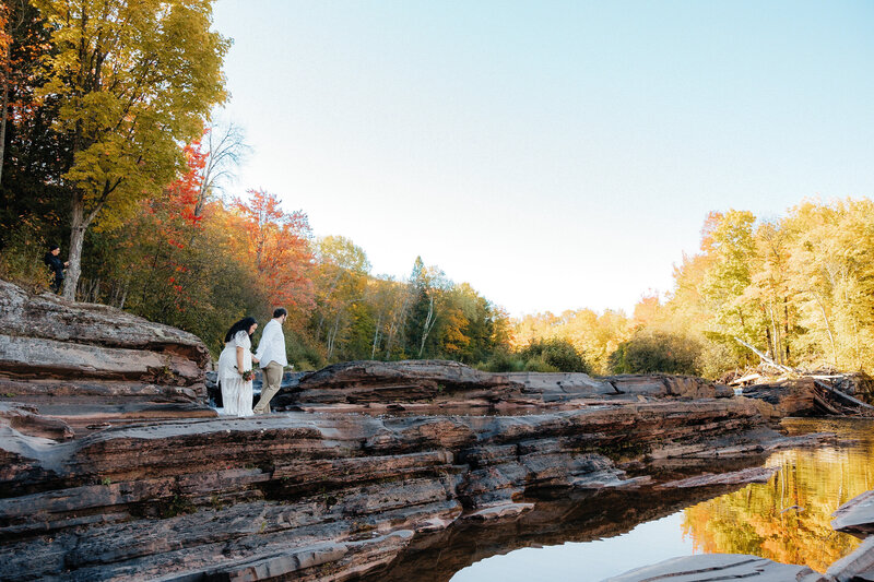 bride and groom sitting on rocks with Lake superior in the background and tall, green, pine trees