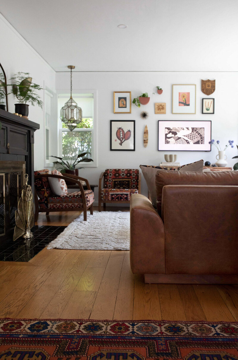 View of living room featuring a brown leather couch, decorative chairs, and artwork on the walls.