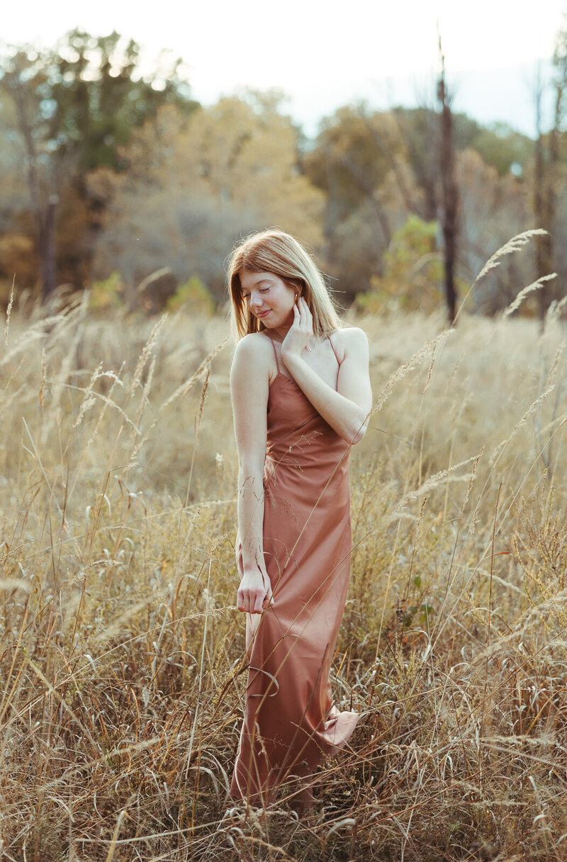 Senior girl in a flowy dress standing in a beautiful field of tall grass. 