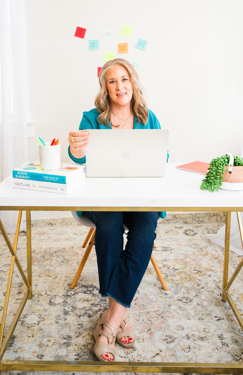 Woman sitting at desk while opening laptop and smiling.