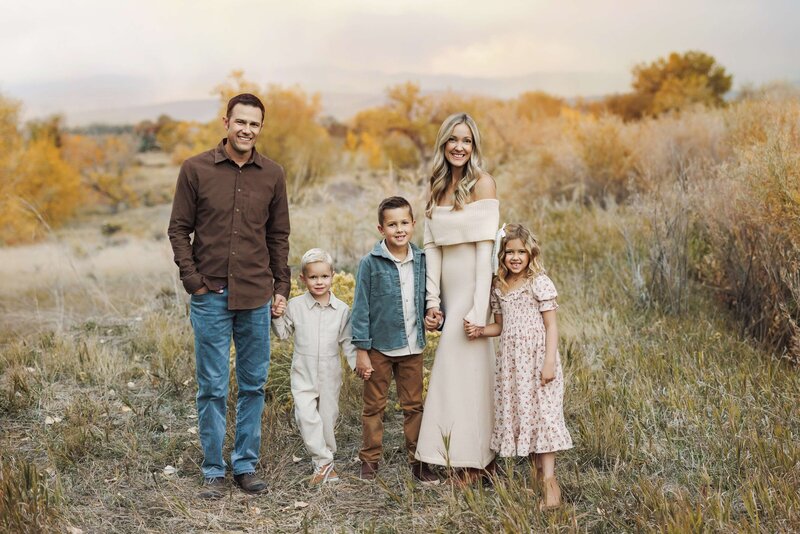 Young family stands together in a field for fall family photos in Denver Colorado