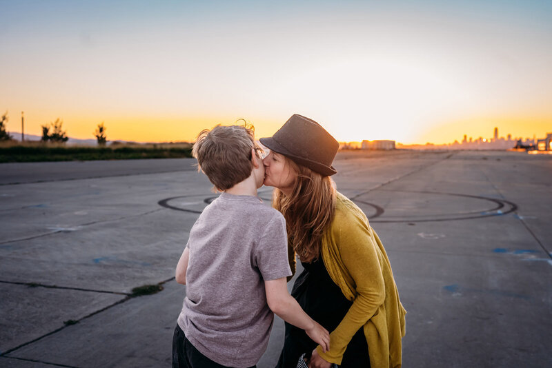 woman wearing a hat and leaning in to kiss her son at Alameda Naval Base