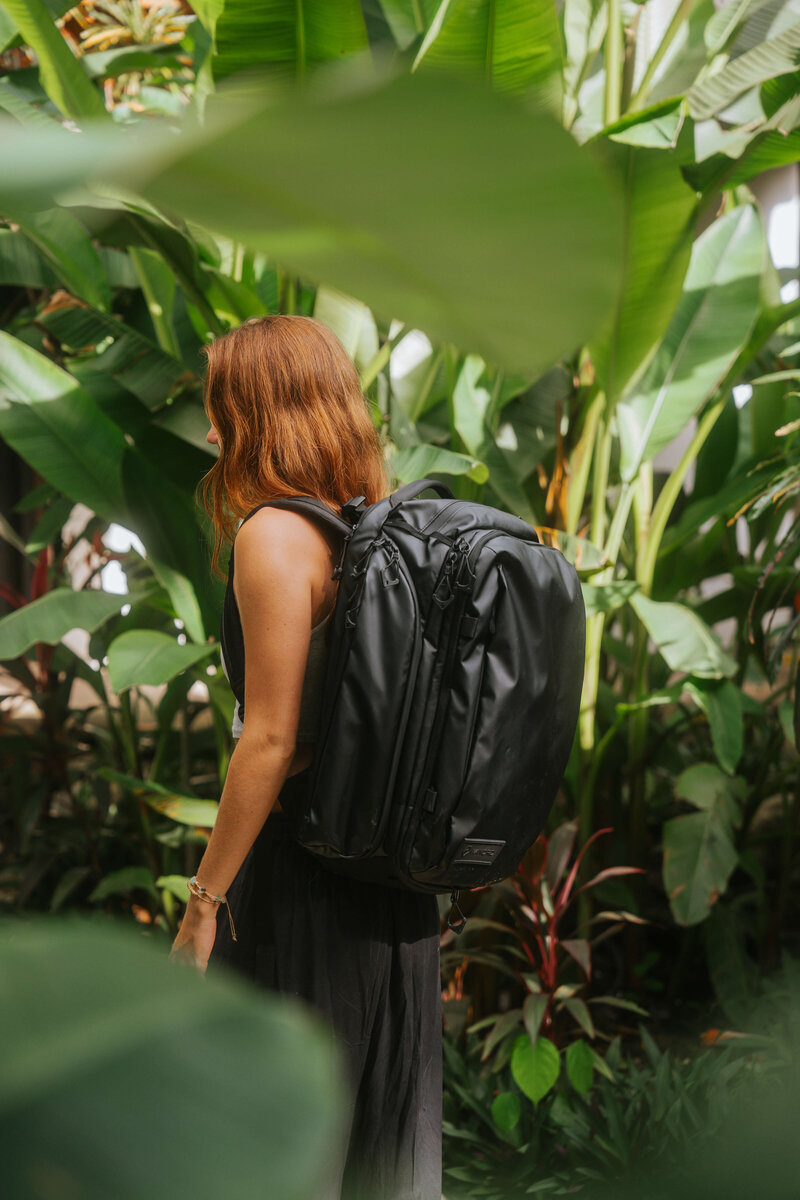 Girl with black travel backpack in greenery