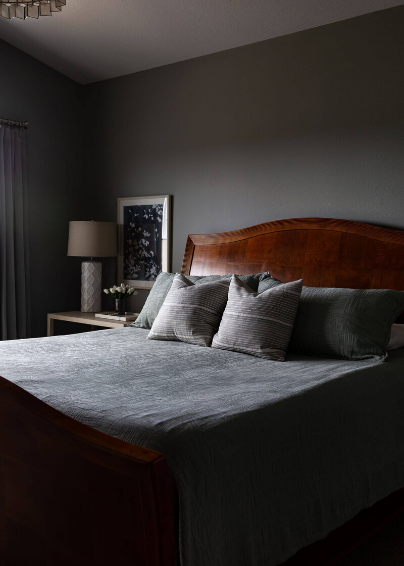 Cozy bedroom with dark walls, wood furniture, and neutral bedding, showcasing modern farmhouse interior design with subtle elegance and soft lighting.