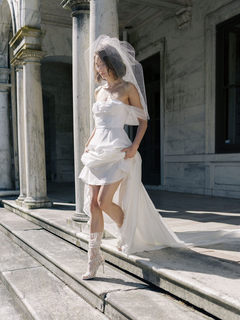 Bride lifting wedding dress skirt walking down mansion stairs