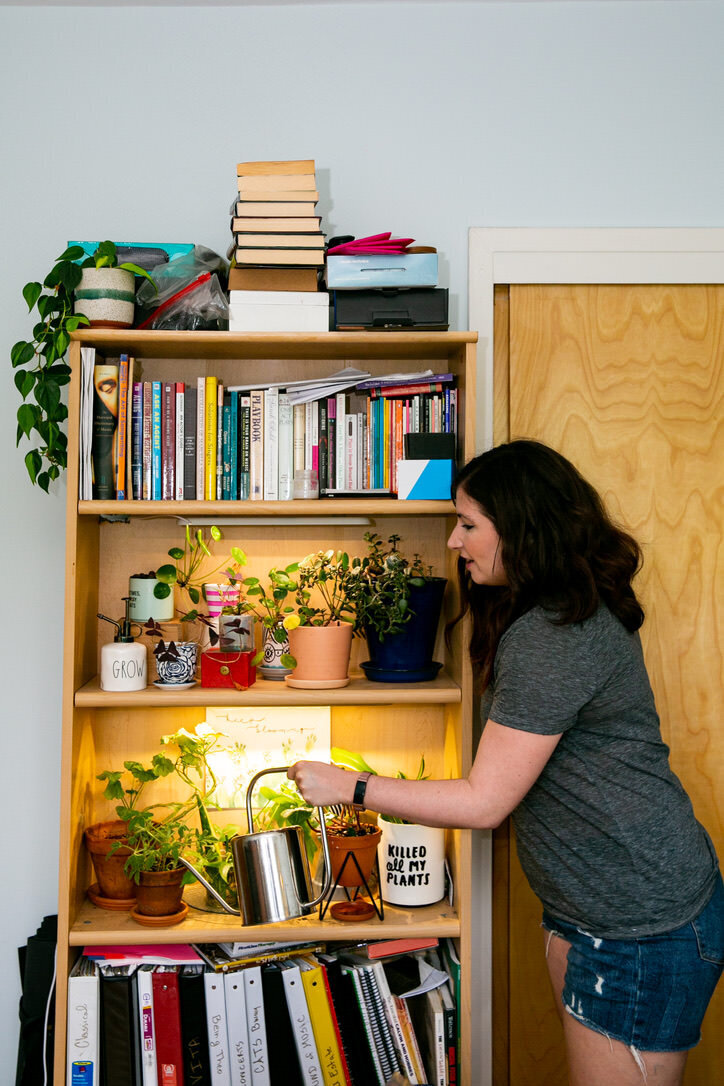 Woman watering houseplants on a bookshelf, lit by ModSprout grow lights
