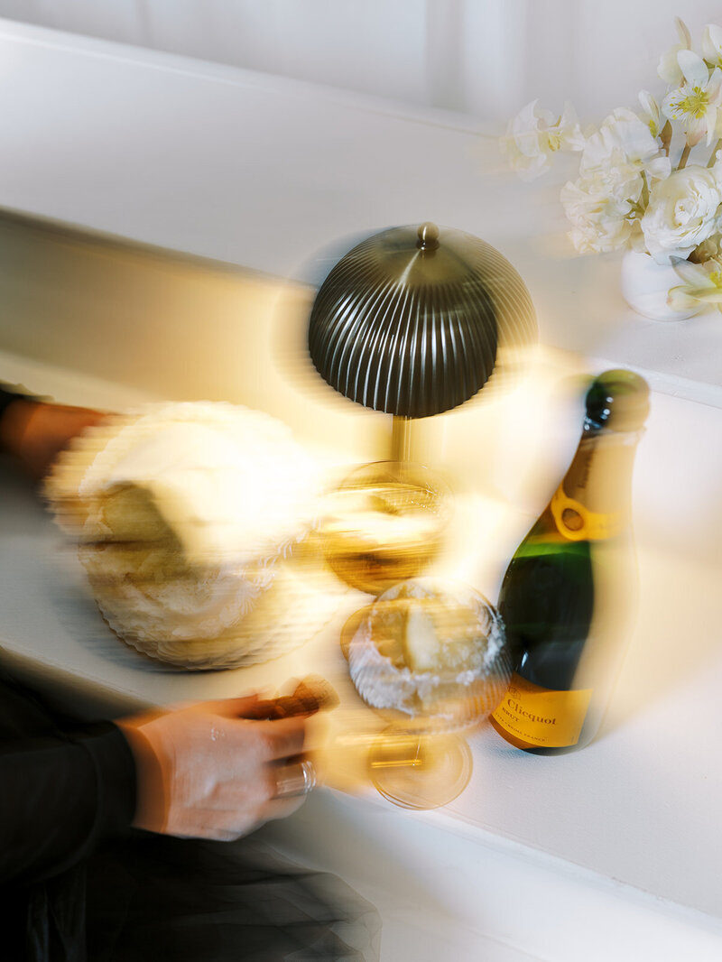 A blurry image of a light, business card and champagne bottle, representing a playful styled photoshoot. 