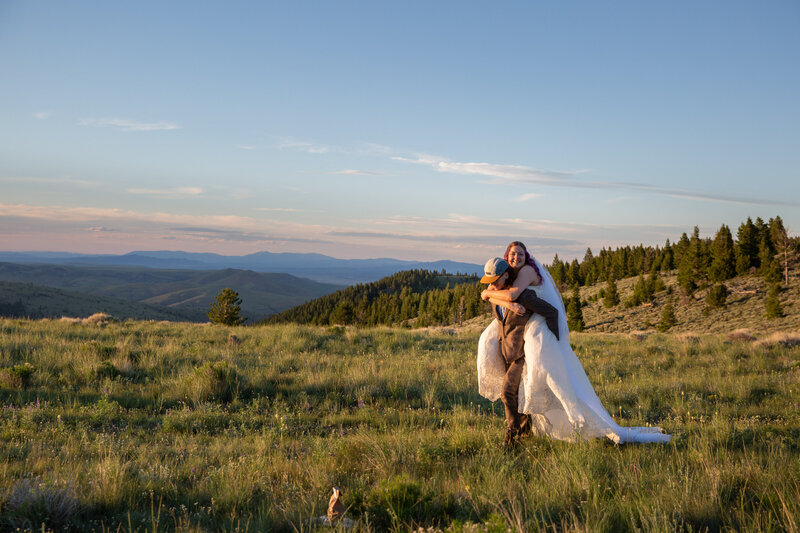 Groom gives his bride a piggy back ride  back to the helicopter in the fading light of a Montana sunset.