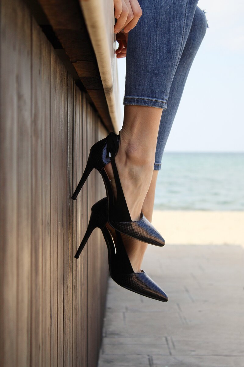 a pair of legs dangling down on a boardwalk at the beach wearing jeans and a pair of black high heels socialfizz