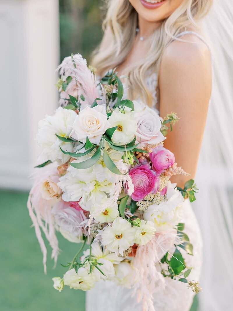 bride looks back an smiles holding white and pink bouquet
