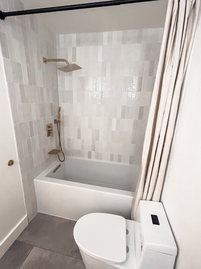 Vertical White and Grey Shiny tiles with a deep white modern soaking tub and gold hardware
