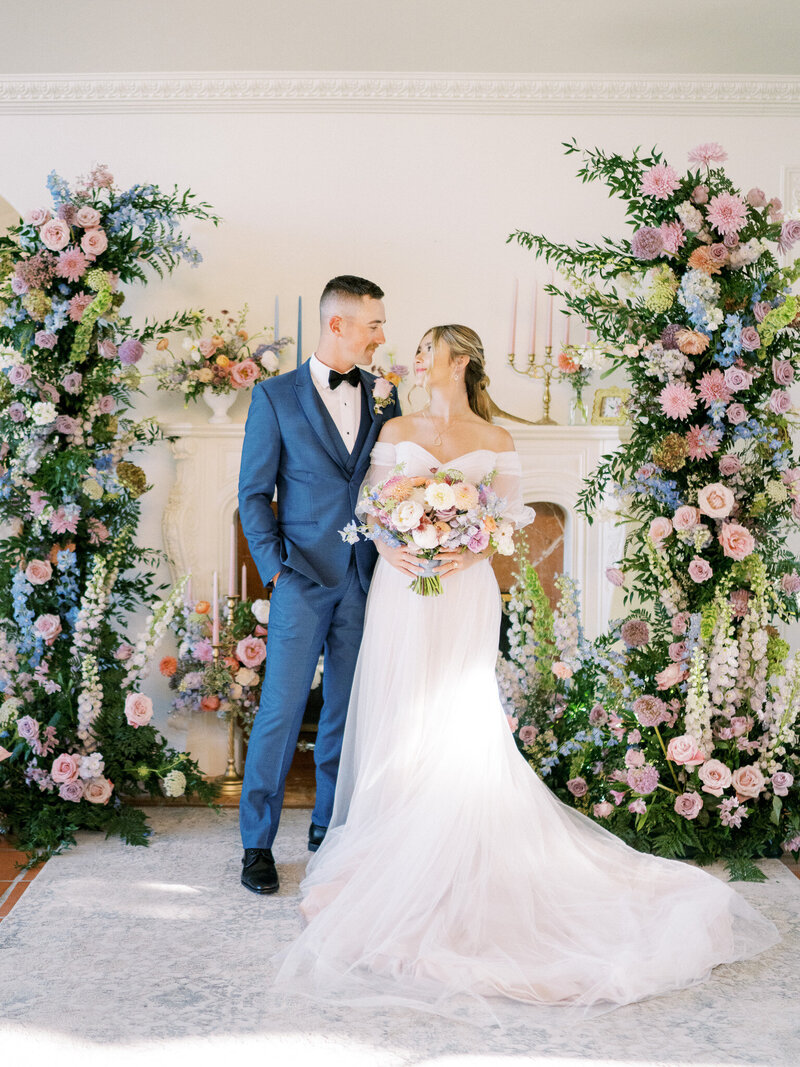 Bride and groom standing in front of a wall full of overflowing flowers during their luxury wedding day in San Luis Obispo