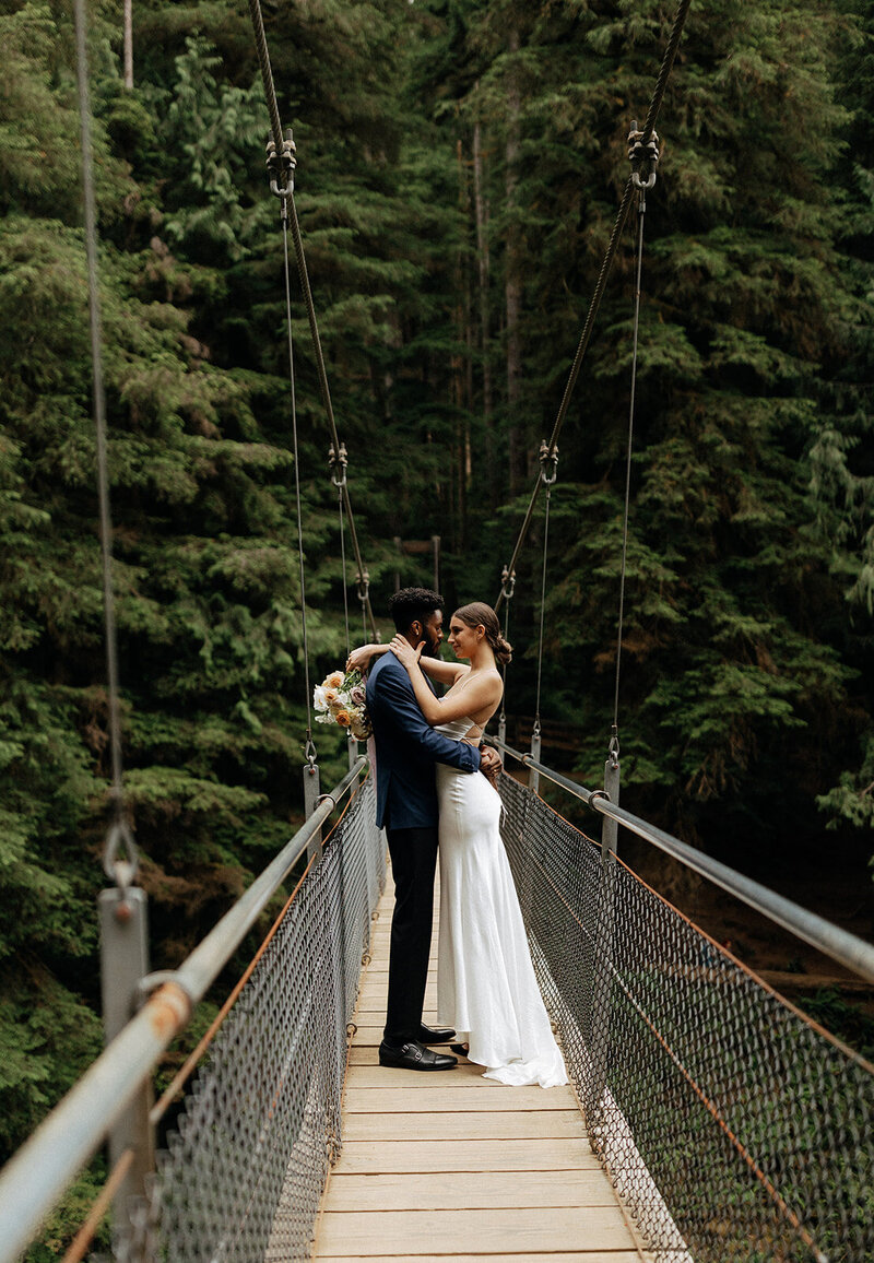 Bride and groom sharing a kiss on a suspension bridge in the Pacific Northwest forest during their elopement.