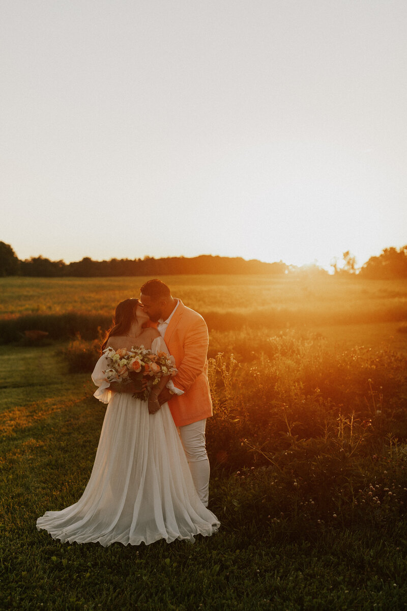 Bride and groom kiss with a bridal bouquet. Gorgeous warm sunset