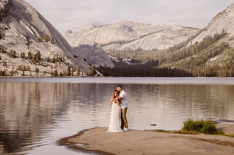 Couple holding each other on the shoreline of Tenaya Lake with granite mountains behind them