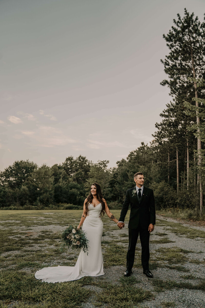 Bride and Groom standing in field by the woods