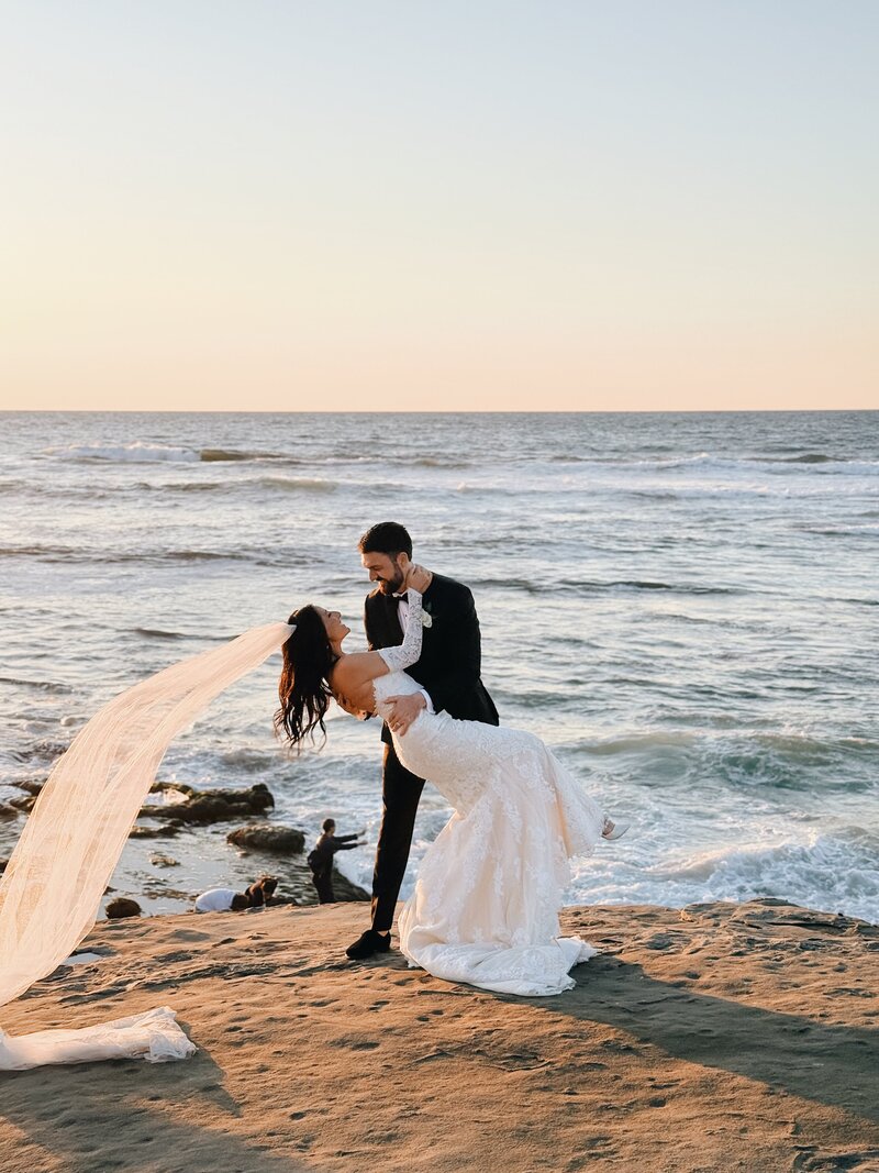 Bride and groom doing a dance dip on the cliffs of La Jolla Beach in San Diego, California.