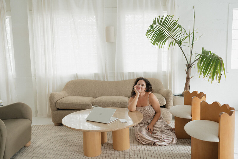 Morgan carrying a laptop and coffee cup by a table