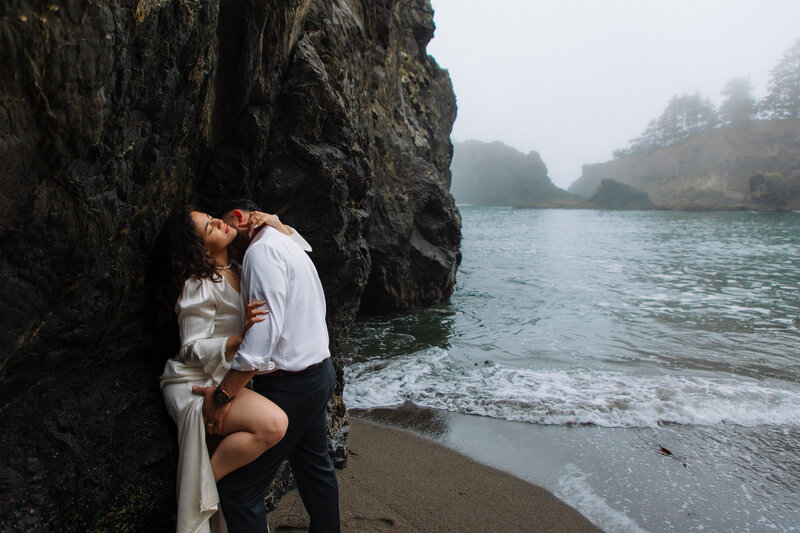 Couple embracing by rugged coastal cliffs with ocean views, photographed by an Oregon Coast Elopement and Wedding Photographer.