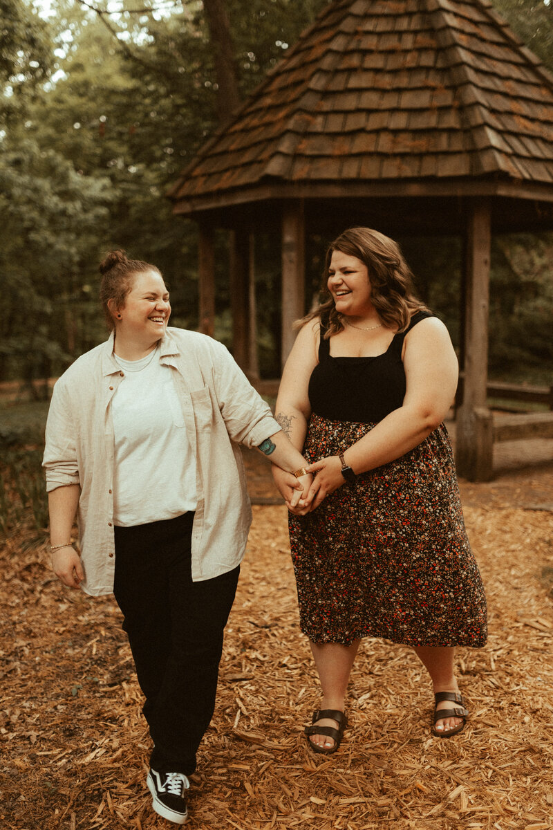 lesbian couple walks hand in hand at mt airy forest for cincinnati engagement photos