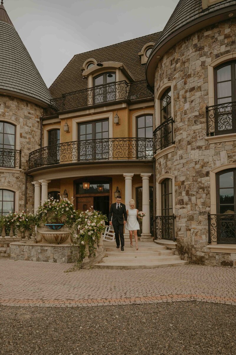 Bride and groom walking down castle steps hand in hand smiling