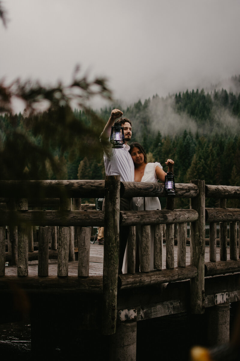 Bride and groom holding lanterns  up with the PNW trees in the background with fog rolling over.