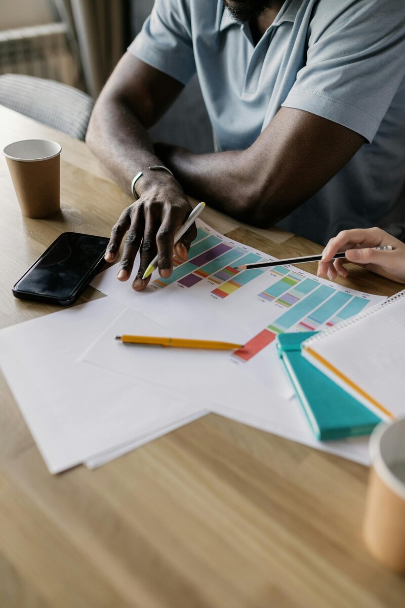 A black man and white woman sit at a desk, reviewing printed graphs.
