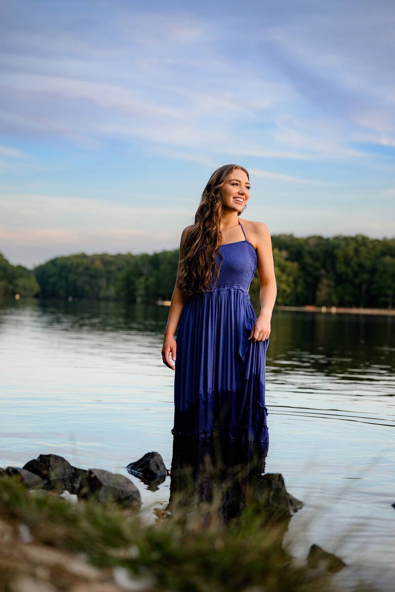 full portrait of a charlotte area graudate looking off camera smiling while standing in a body of water 
